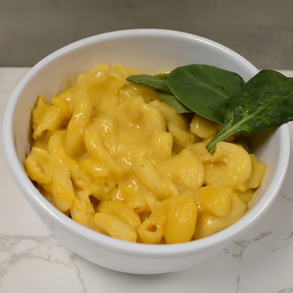 A white bowl filled with creamy macaroni and cheese, garnished with fresh spinach leaves.