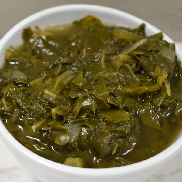 Close-up of a white bowl filled with Fat Man's BBQ collard greens, featuring tender green leaves and broth.