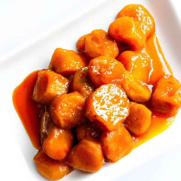 Close-up of Fat Man's BBQ candied yams, glistening with sweet syrup on a white plate.